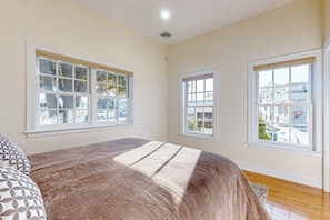 A bedroom with a large bed, two windows, and a view of the street.