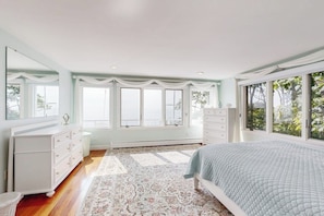 A bedroom with a bed, dresser, and large windows.
