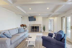 A living room with a sofa, armchair, fireplace, television, and large windows.