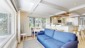 Una sala de estar moderna con un sofá azul, un comedor con sillas blancas y una cocina con armarios blancos.