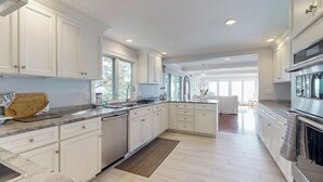 Una cocina moderna con armarios blancos, una isla central y vista al área de estar.