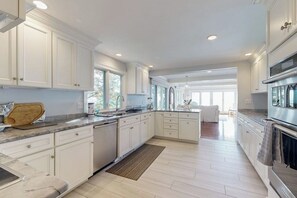A modern kitchen with white cabinetry, a central island, and a view to the living area.