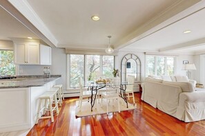 A spacious living area with a kitchen, a dining table with chairs, a sofa, and a large window providing natural light.