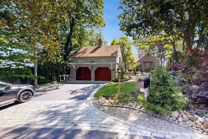 A residential driveway leading to a house with a garage, surrounded by trees and a well-maintained garden.