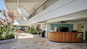 Un espace d’accueil doté d’un comptoir en bois, d’un ventilateur de plafond et offrant une vue sur le patio extérieur, agrémenté de plantes et d’un coin salon.