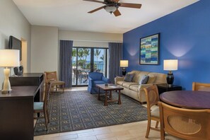 A hotel room with a ceiling fan, a sofa, a coffee table, a TV, and a view of the ocean through large windows. - Oceanfront, modern in Kailua-Kona. It’s ideal for all of your island adventures. (Kailua-Kona)