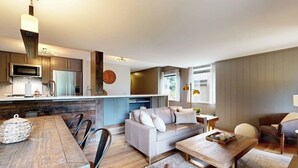 A modern kitchen with a central island, a dining area with a wooden table, and a living space with a sofa and a coffee table. - Gorgeous mountain retreat with pool, hot tub, games, & golf - walk-to-lifts (Sun Valley)