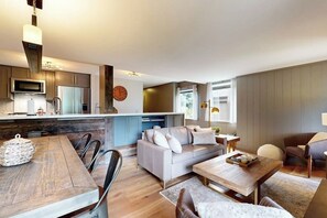 A modern kitchen with a central island, a dining area with a wooden table, and a living space with a sofa and a coffee table. - Gorgeous mountain retreat with pool, hot tub, games, & golf - walk-to-lifts (Sun Valley)