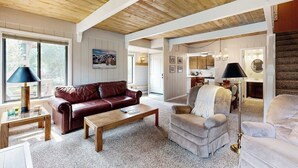 A spacious living area with a wooden ceiling, a brown leather sofa, a beige armchair, and a coffee table. - Charming condo with WiFi, deck, fireplace, shared pool, hot-tub, and sauna (Sun Valley)