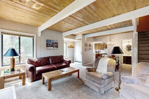 A spacious living area with a wooden ceiling, a brown leather sofa, a beige armchair, and a coffee table. - Charming condo with WiFi, deck, fireplace, shared pool, hot-tub, and sauna (Sun Valley)