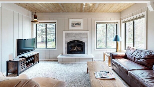 A living room with a fireplace, television, and leather sofa. - Charming condo with WiFi, deck, fireplace, shared pool, hot-tub, and sauna (Sun Valley)