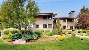 A modern two-story house with a well-maintained garden, a visible deck, and a clear sky. - Charming condo with WiFi, deck, fireplace, shared pool, hot-tub, and sauna (Sun Valley)