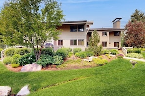 A modern two-story house with a well-maintained garden, a visible deck, and a clear sky. - Charming condo with WiFi, deck, fireplace, shared pool, hot-tub, and sauna (Sun Valley)