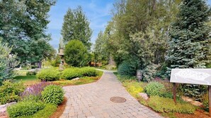 A paved garden pathway surrounded by various shrubs and trees. - Charming condo with WiFi, deck, fireplace, shared pool, hot-tub, and sauna (Sun Valley)