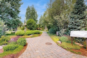 A paved garden pathway surrounded by various shrubs and trees. - Charming condo with WiFi, deck, fireplace, shared pool, hot-tub, and sauna (Sun Valley)