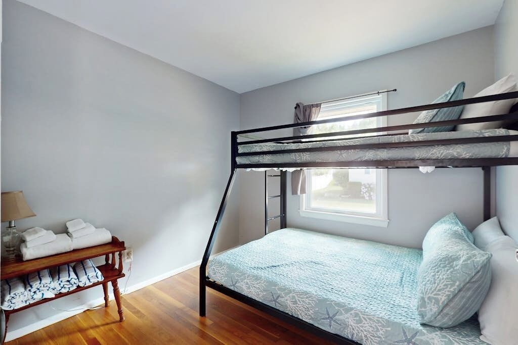 Dormitorio con literas, una ventana, un banco de madera con toallas y una lámpara.