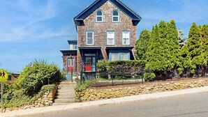 A two-story wooden house with a front porch, a stone retaining wall, and a metal fence. - Beautifully renovated home walk to boulevard, town & train (Gloucester)