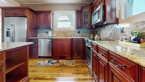A kitchen with wooden cabinets, a stainless steel refrigerator, a microwave, and a dishwasher. - Beautifully renovated home walk to boulevard, town & train (Gloucester)