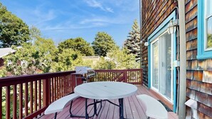 A wooden deck with a round table and chairs, a grill, and a view of trees and a building. - Beautifully renovated home walk to boulevard, town & train (Gloucester)