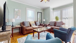 A living room with a brown leather sofa, a blue armchair, a wooden coffee table, and a ceiling fan. - Beautifully renovated home walk to boulevard, town & train (Gloucester)