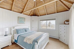 Een slaapkamer met een houten plafond, een bed met gestreept beddengoed, een nachtkastje, een kast en een raam met uitzicht.