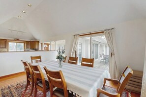 Een eethoek met een tafel voor zes personen, houten stoelen, een vaas met bloemen en uitzicht door een groot raam.
