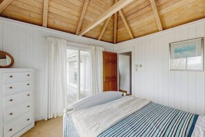 A bedroom with a wooden ceiling, a bed with striped bedding, a white dresser, and a door leading outside. - Private beachfront escape on Coffins Beach w/ amazing views & private beach (Gloucester)