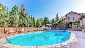 A swimming pool with lounge chairs, a wooden deck, and a building with a sloped roof. - Cozy ski condo with patio, fireplace, WiFi, shared pool & hot tub, walk to lifts (Sun Valley)