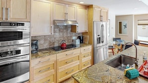 A modern kitchen with stainless steel appliances, wooden cabinets, and a granite countertop. - Cozy ski condo with patio, fireplace, WiFi, shared pool & hot tub, walk to lifts (Sun Valley)