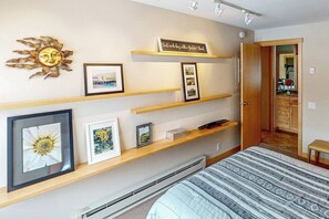 Ein Schlafzimmer mit einem Bett, einem an der Wand befestigten Regal mit gerahmten Bildern, einer Sonnendekoration und einer Tür zu einem Badezimmer.
