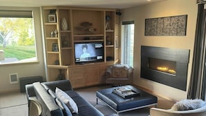 A modern living room with a sofa, armchair, TV, fireplace, and built-in shelving. - Cozy ski condo with patio, fireplace, WiFi, shared pool & hot tub, walk to lifts (Sun Valley)