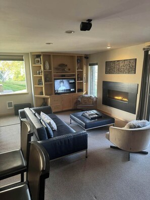 Ein modernes Wohnzimmer mit Sofa, Sesseln, Fernseher, Kamin und Einbauschränken.