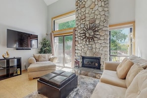 Una sala de estar con chimenea, televisor de pantalla plana, sofá y pared de piedra.