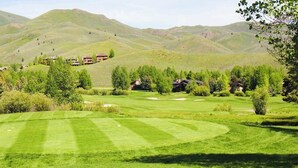 Un parcours de golf avec des collines douces et quelques bâtiments visibles au loin.