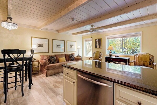 Una cocina con techo de madera, una zona de comedor con mesa y sillas, un sofá y cuadros en las paredes.