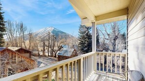 Eine Holzterrasse mit einem Stuhl, Blick auf die Berge und eine kleine Holzhütte im Hintergrund.