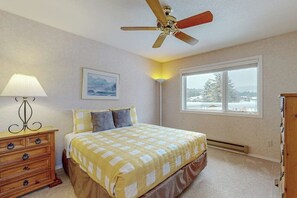 A bedroom with a bed, a nightstand, a lamp, a ceiling fan, a window with a view, and a wall-mounted picture. - Spacious Dog-Friendly Condo on the 7th Hole of Eagle Bend Golf Course (Bigfork)