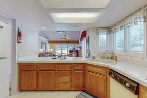 A kitchen with wooden cabinets, a dishwasher, and a window with curtains. - Spacious Dog-Friendly Condo on the 7th Hole of Eagle Bend Golf Course (Bigfork)