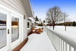 A covered deck with a table and chairs, a white railing, and a snowy landscape in the background. - Spacious Dog-Friendly Condo on the 7th Hole of Eagle Bend Golf Course (Bigfork)