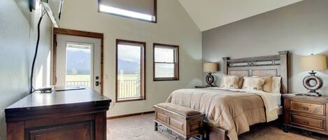 A bedroom with a bed, nightstands, a dresser, and a desk. There are three windows providing natural light and a view of the outdoors.