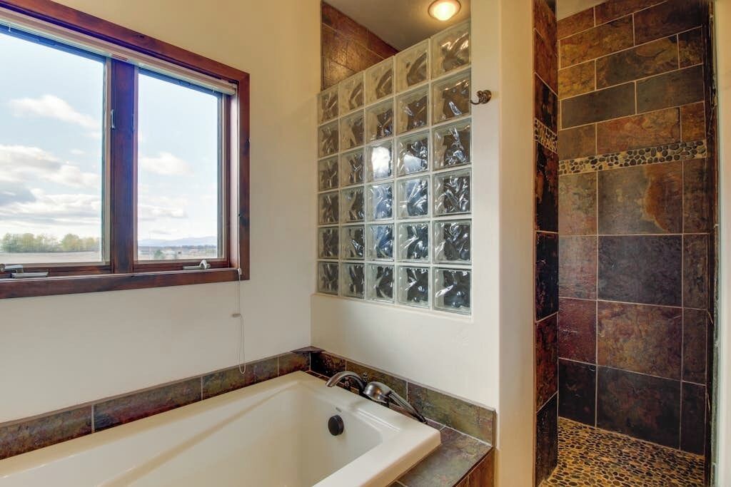 A bathroom with a bathtub, a window, and a shower area with tiled walls.