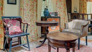 A room with a vintage chair, a round wooden table, and floral curtains.