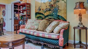 A cozy living room with a sofa, a round wooden table, a bookshelf, and a decorative lamp.