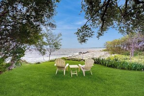 Un espacio al aire libre con césped, dos sillas y una mesa, con vistas a una costa rocosa.