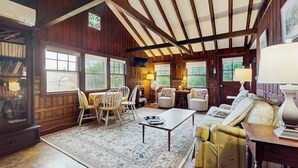 Ein gemütliches Zimmer mit Holzwänden, einem großen Fenster, einer Couch, einem Tisch und einem Bücherregal.