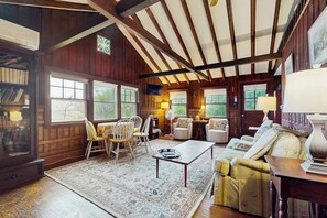 Una habitación acogedora con paredes de madera, un ventanal grande, un sofá, una mesa y una estantería.