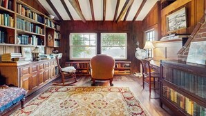 Ein Zimmer mit Holzbögen, einem Klavier, einem Sessel und einem großen Fenster.