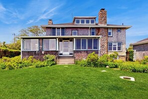A two-story house with a stone chimney, large windows, and a well-maintained lawn.