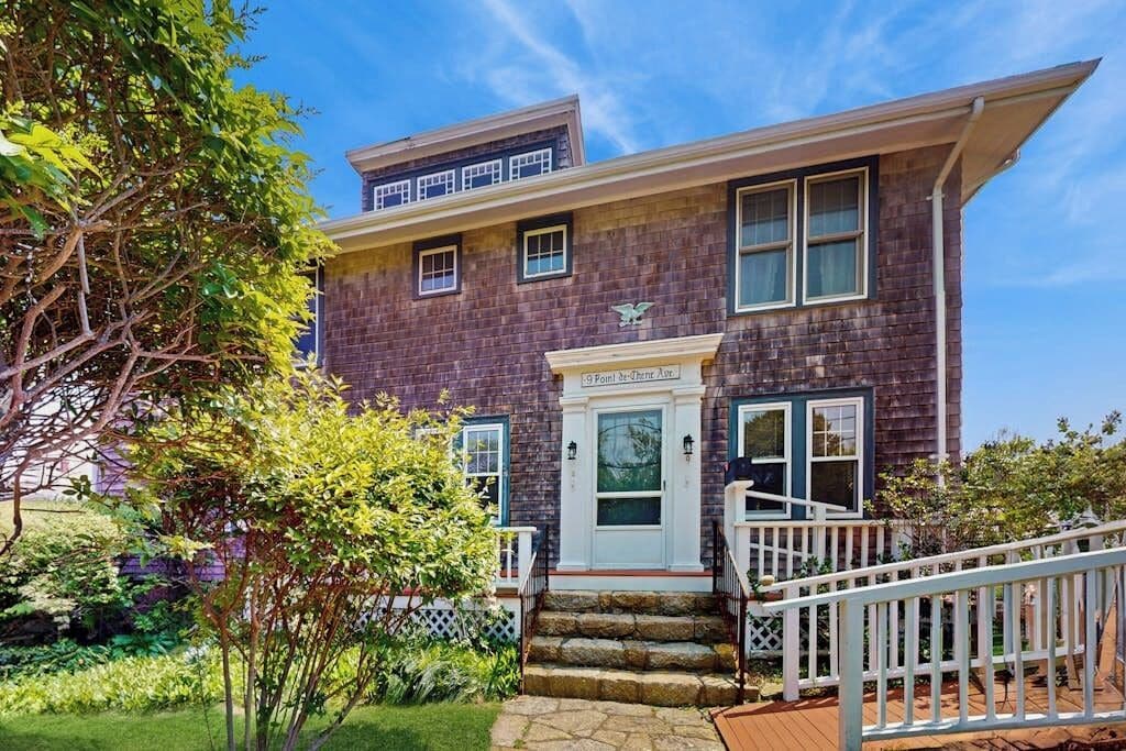 Une maison à deux étages avec un porche à l’avant, une petite terrasse et une façade en briques.