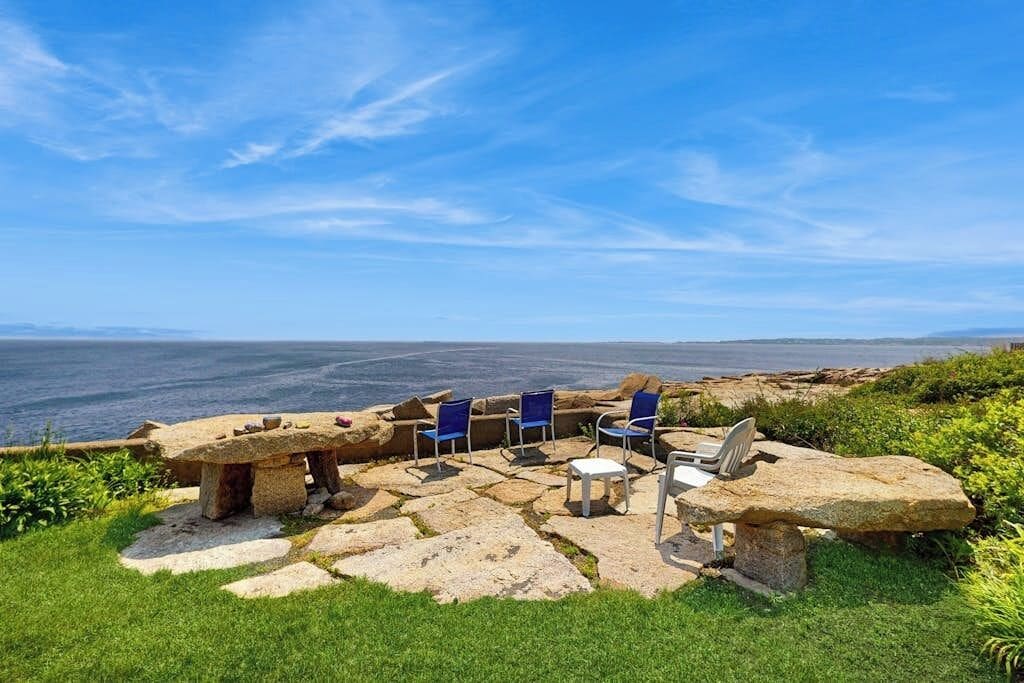 Une terrasse en pierre avec des sièges extérieurs et une vue sur la mer.